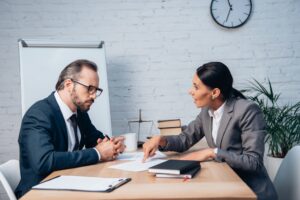 businesswoman pointing with finger at document and talking with coworker in glasses