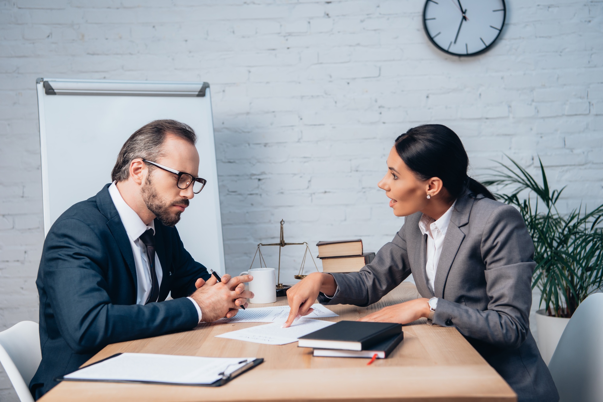 businesswoman pointing with finger at document and talking with coworker in glasses