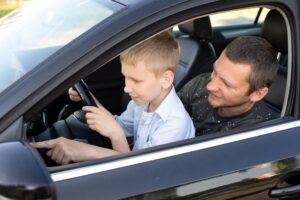 Dad and son in the front seat of a car driving a black car.