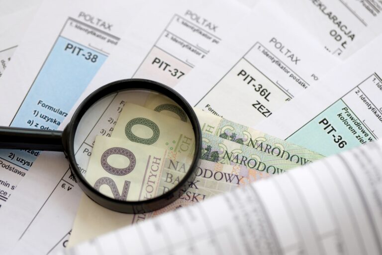 Polish zloty money and magnifying glass on big amount of polish tax forms close up. Accounting