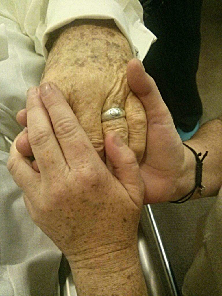 Vertical image of daughter holding aging hand of father on his death bed.