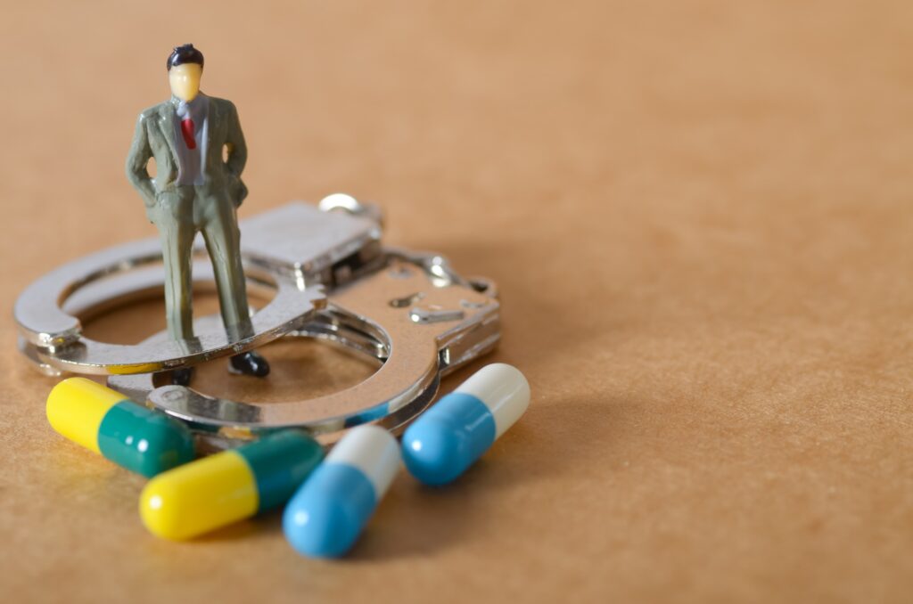 Businessman Figurine Standing on Handcuffs with Scattered Pills – Crime and Drug Concept